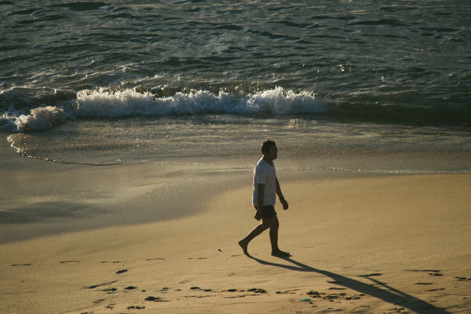 Man walking the shoreline at dawn, first light on the water